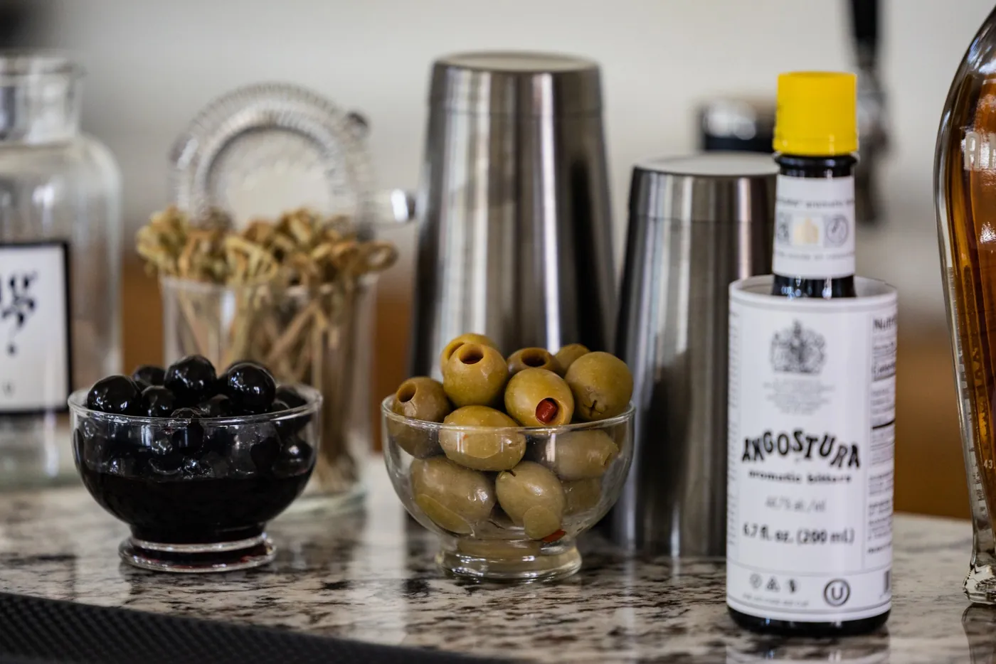 Bowls of black and green olives on a marble counter with a bottle