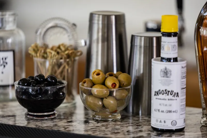 Bowls of black and green olives on a marble counter beside a bottle